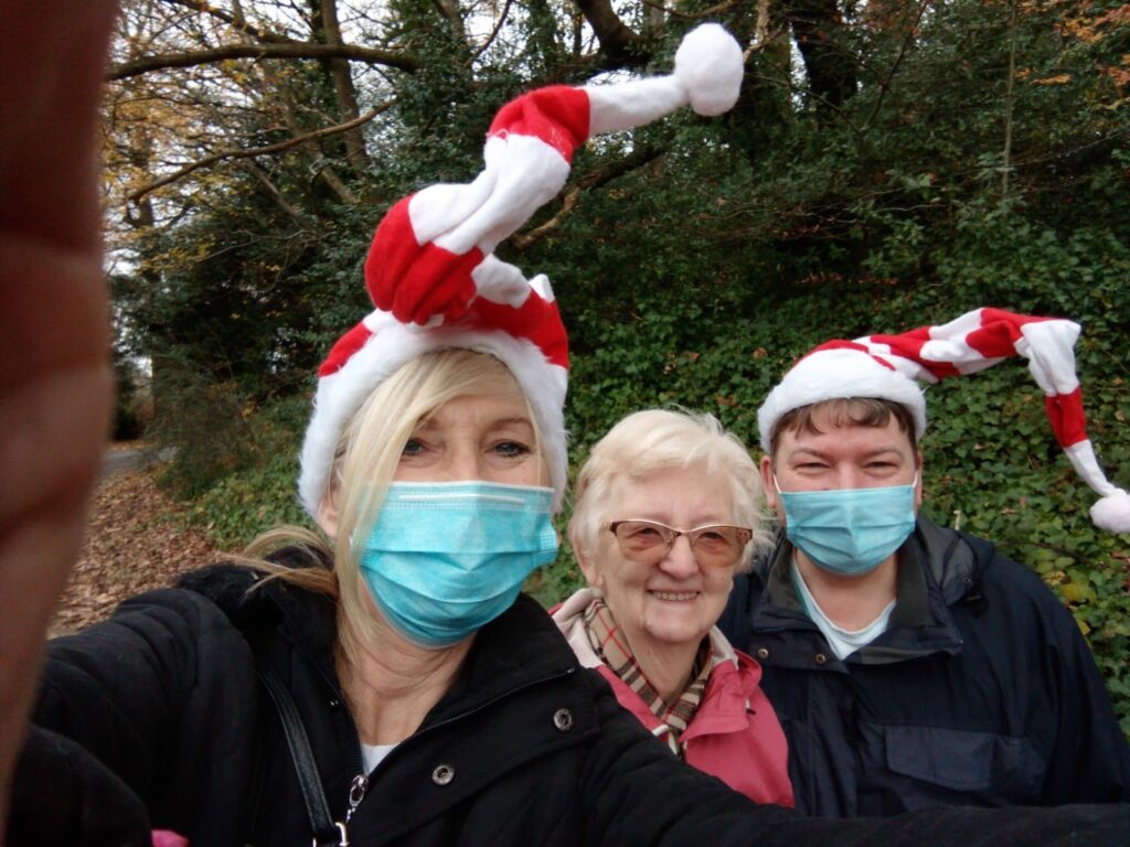 A resident smiling with two members of the team who are wearing festive hats
