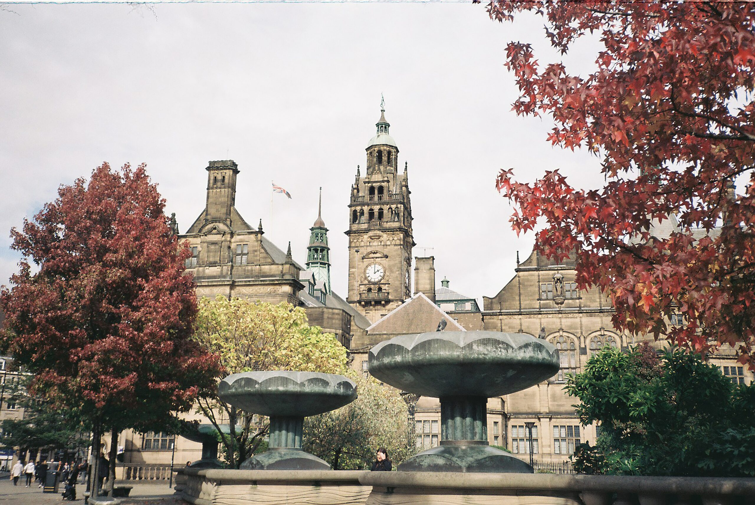 Clock tower and fountain located in Sheffield with red trees surrounding.