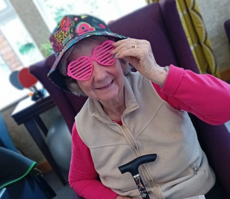 resident sat down in a purple armchair wearing pink love heart glasses