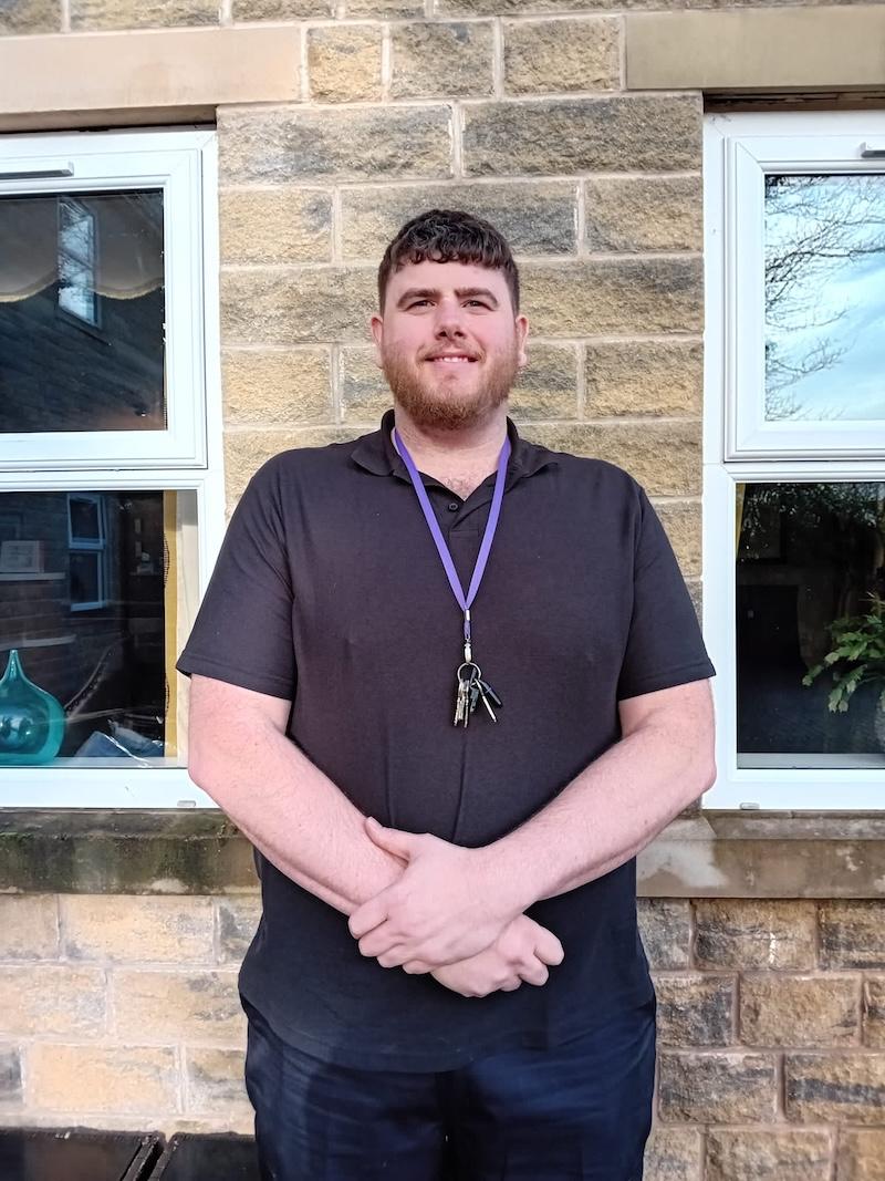 Man with brown hair stood in front of a brick wall for a headshot for the team page