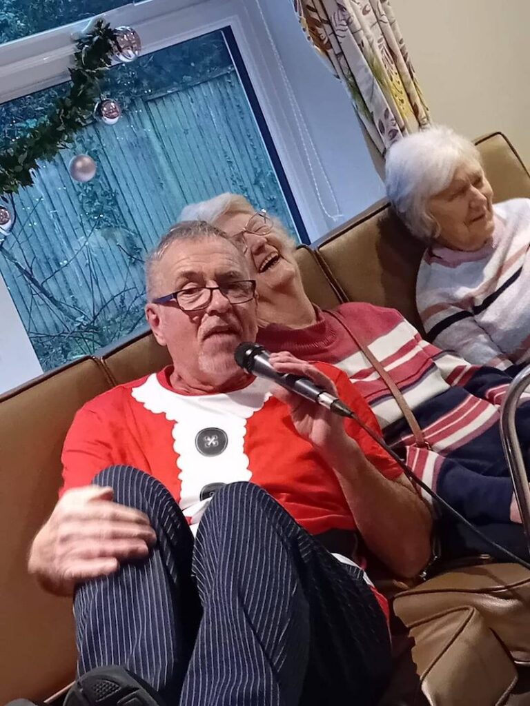 entertainer sat with residents in a christmas outfit singing to them