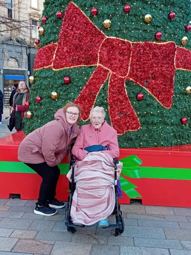 resident and carer stood in front of a big christmas tree in sheffield town centre smiling