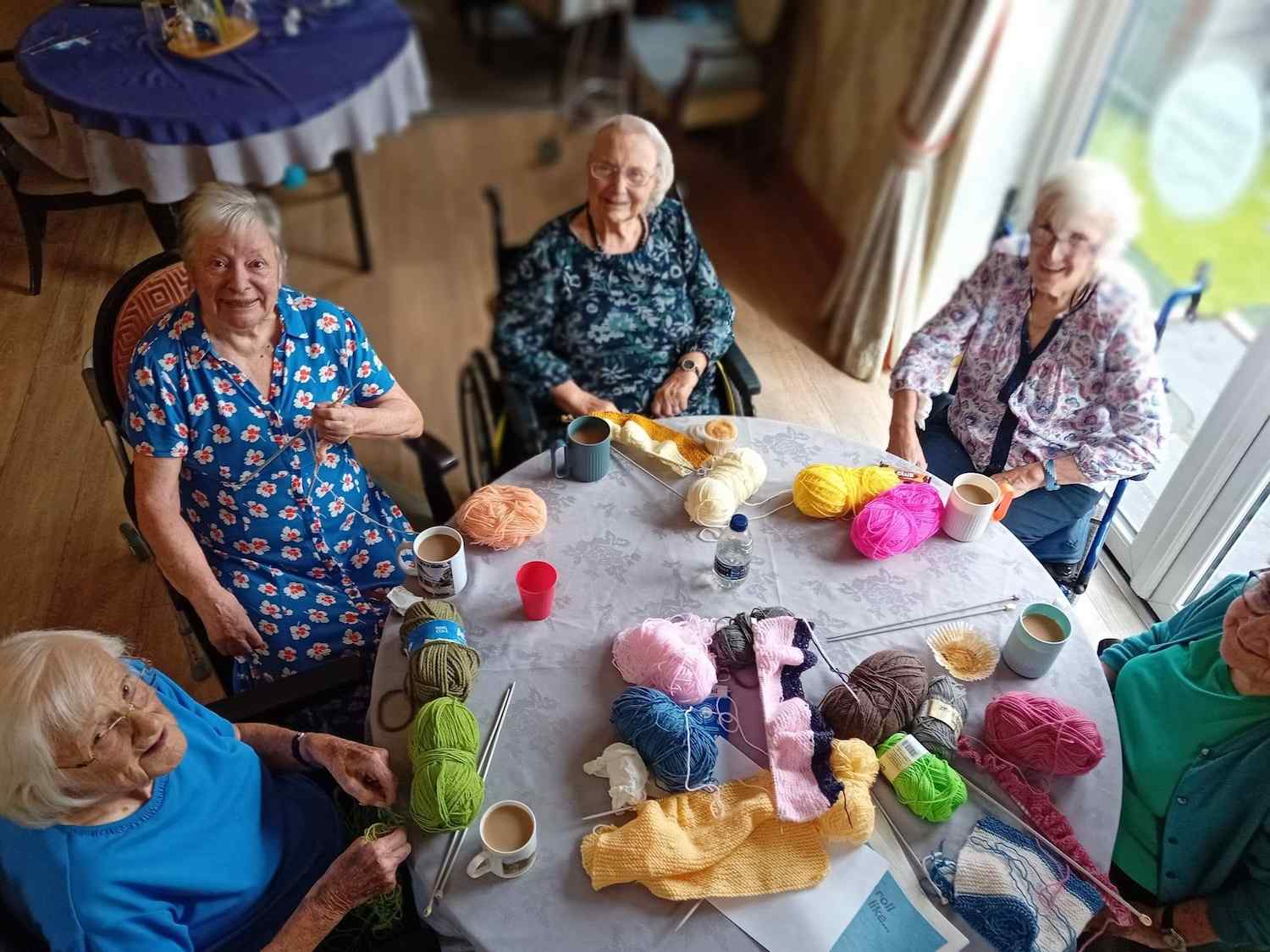 a group of our residents sat around the table together knitting with cups of tea